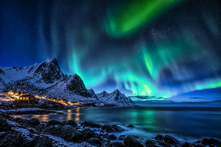 Northern lights above a shoreline with defined landscape details.